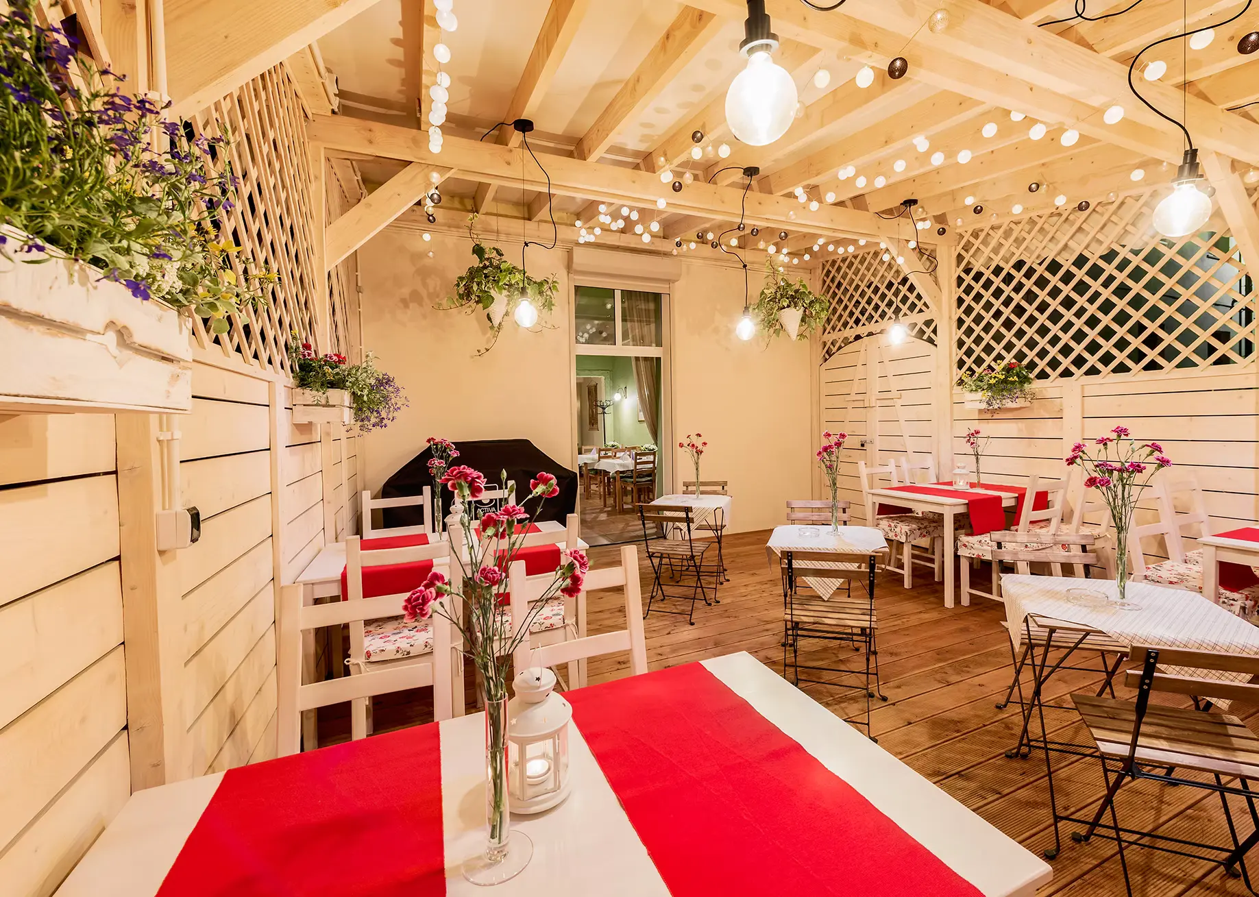 Letnie patio - stoliki z kwiatami i girlandami świetlnymi